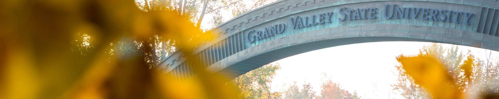 A look at the GVSU welcome bridge at the entrance of campus through fall leaves